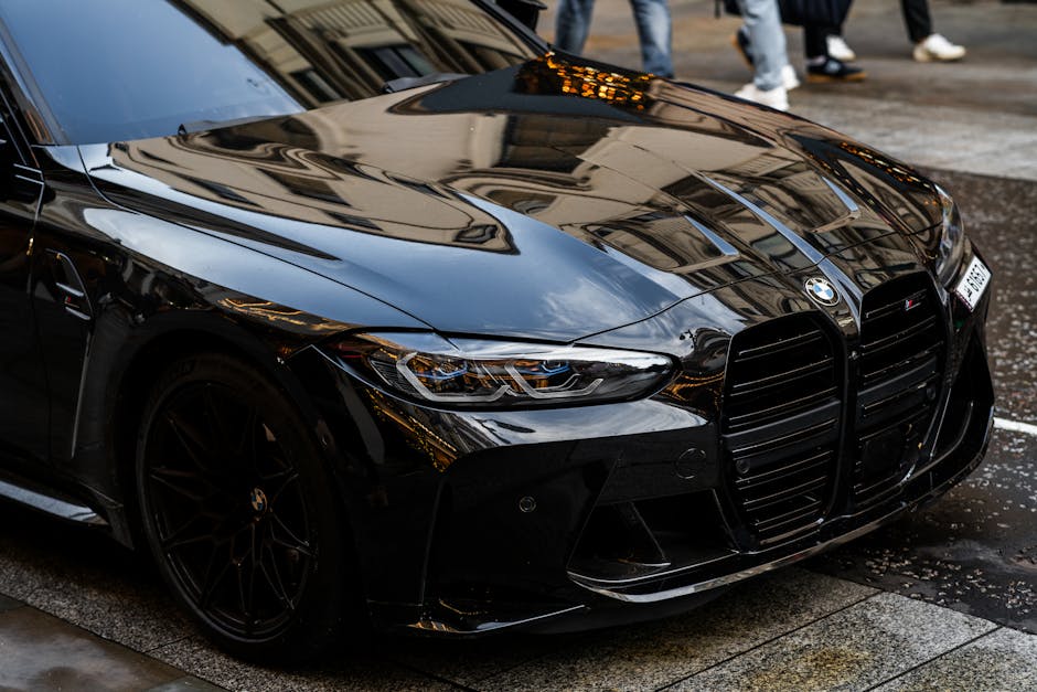A sleek black BMW M4 parked on a rainy London street, showcasing its luxury design.