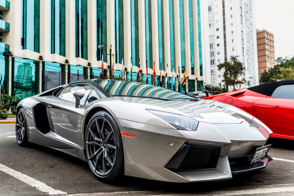 Luxury silver sports car parked in front of modern glass facade building.