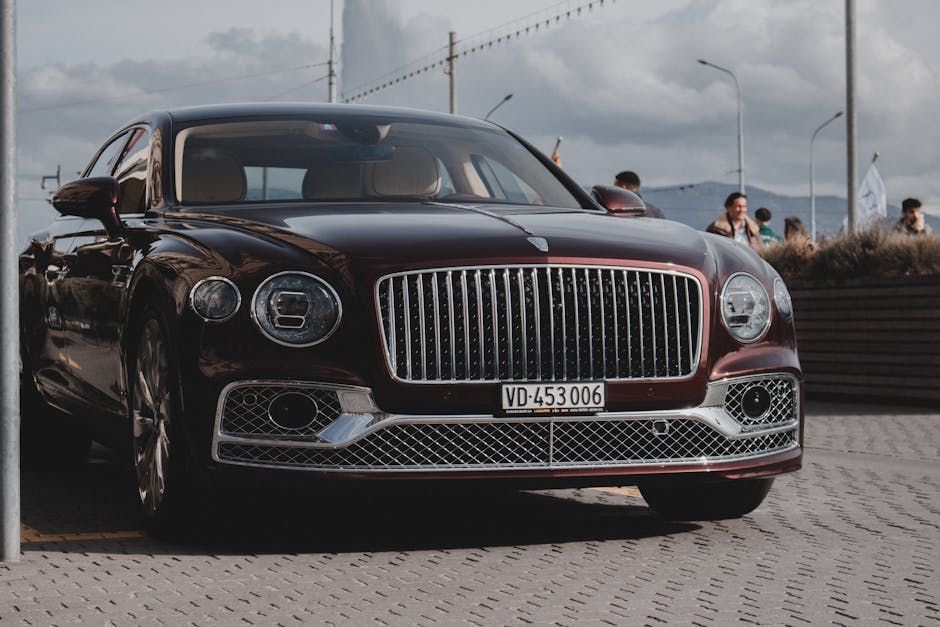 Front view of a shiny luxury Bentley car parked outdoors with people in the background.